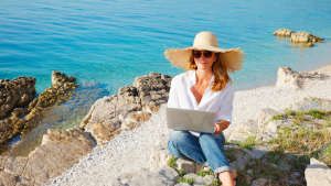 Woman sitting with a laptop on the top of a sea cliff. 